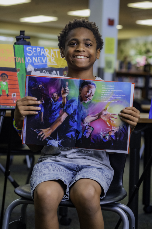 Smiling boy holding up a book.